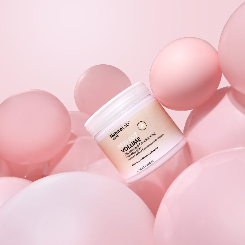 Photo of Perfect Volume Thickening & Conditioning Hair Masque surrounded by pale pink round balloons. The product jar is tilted at a 45-degree angle to the left. The photo feels playful and whimsical in a minimalist way.