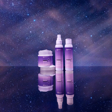 All three Perfect Dream products -- the Night Repair Masque, the Good Night Anti-Static Pillow Mist, and the Calming Bath Oil -- arranged in a line, in front of a midnight-blue and purple-pink starry background. The horizon marks where the products and the starry sky reflections start, as if the products are sitting on a mirror.
