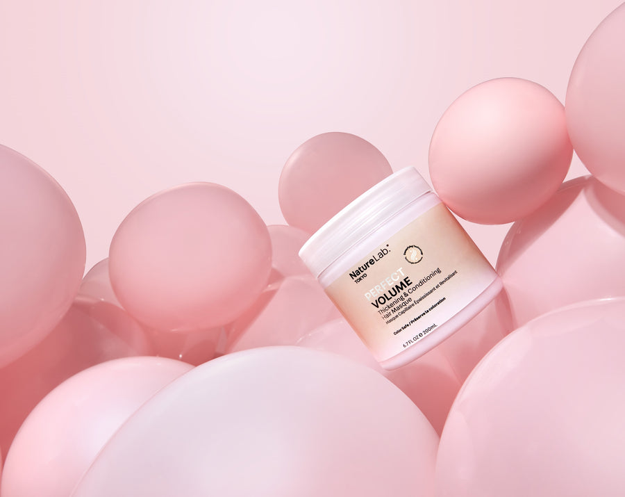 Photo of Perfect Volume Thickening & Conditioning Hair Masque surrounded by pale pink round balloons. The product jar is tilted at a 45-degree angle to the left. The photo feels playful and whimsical in a minimalist way.