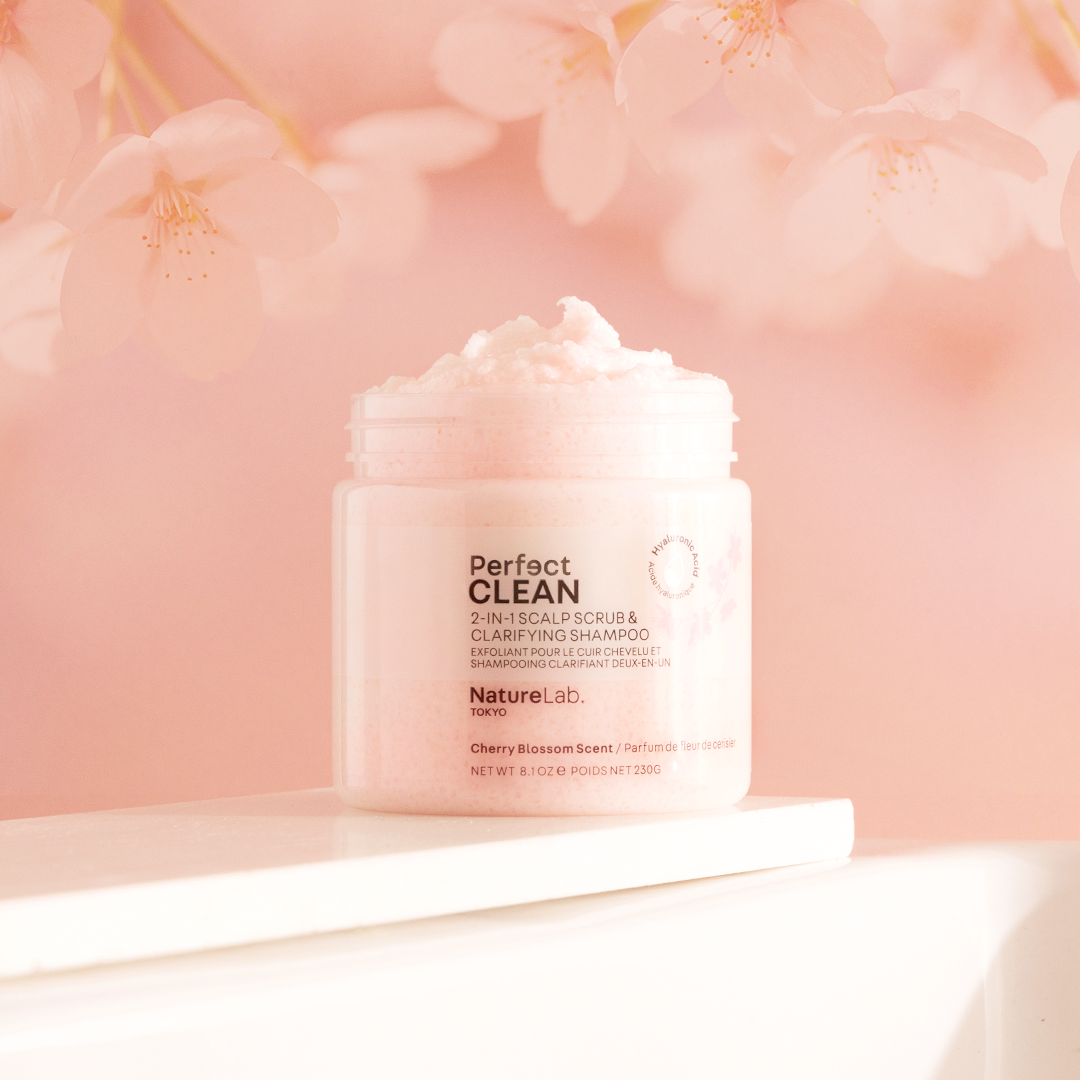 Perfect Clean 2-in-1 Scalp Scrub: Sakura with the jar lid removed to show off the fluffy texture. The background is light pink with a faint image of cherry blossoms.