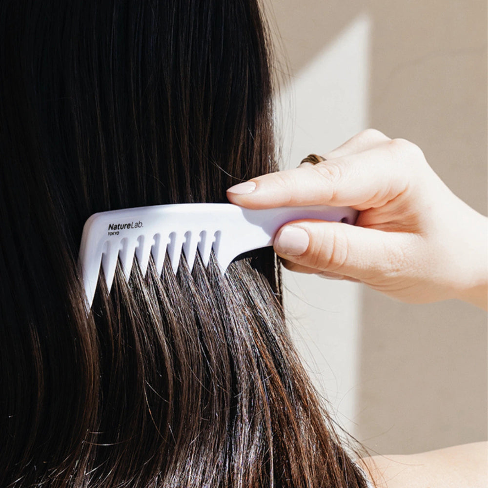 Person using a white detangling comb on dark frizz-free and smooth hair with a neutral background