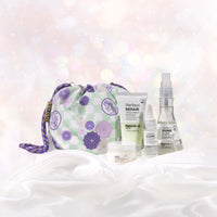 All four products and the NatureLab Tokyo x BYBBA reusable gift bag in the Fan Favorites Holiday Kit arranged together on white satin against a pale sparkly backdrop. The collaboration bag is a pale green and white checker pattern with Japanese-style circular flowers in various shades of purple printed on top, along with a circular stamp pattern that shows a maneki neko (lucky cat) with the text NATURELAB TOKYO above its head.