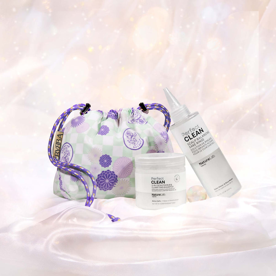 The NatureLab Tokyo x BYBBA reusable drawstring pouch, Perfect Clean 2-in-1 Scalp Scrub & Clarifying Shampoo, and Perfect Clean Scalp Balancing Sake RInse arranged together on white satin with a pale, subtly sparkly background. The BYBBA bag is a pale green and white checker pattern with Japanese-style circular flowers in various sizes and purple shades on top. The pattern also includes a printed stamp in a circle shape with a maneki neko (lucky cat) inside with the text NATURELAB TOKYO over the cat's head.